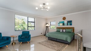 Ein Schlafzimmer mit einem Bett, zwei blauen Sesseln, einem kleinen runden Tisch und einer Stehlampe.