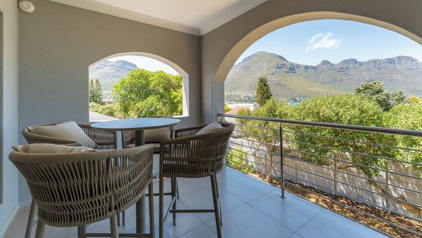 Ein Balkon mit Korbstühlen und einem Tisch, mit Blick auf Berge und Grün.