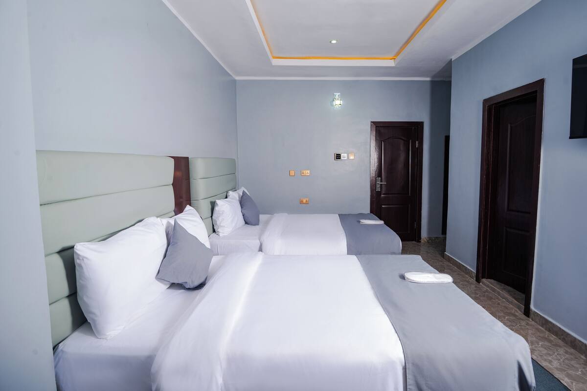 A hotel room with two beds, a headboard, a bedside table, a wall-mounted TV, and a door.