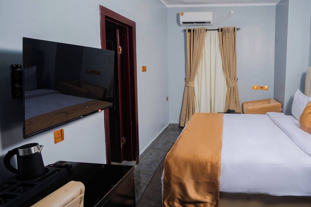 A hotel room with a bed, a television, a coffee maker, and a window with curtains.