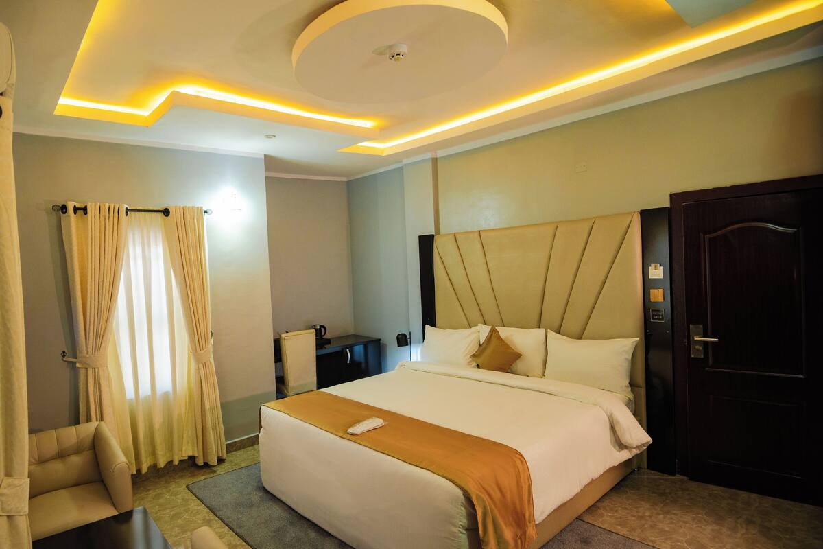 A hotel room with a large bed, a bedside table, a desk, and a wardrobe.