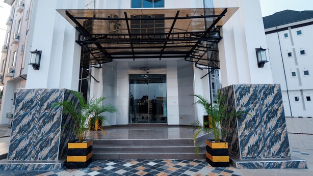 A modern building entrance with a glass door, a covered walkway, and marble steps. - Asato Hotel (Asaba)