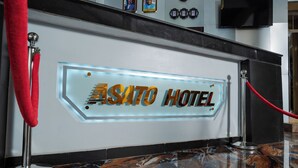 A reception desk with a sign reading "SATO HOTEL" and a red rope barrier. - Asato Hotel (Asaba)