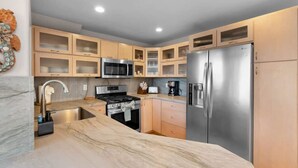 A modern kitchen with a stainless steel refrigerator, a microwave, a stove, and wooden cabinets. - Mission Bay Beach House/Roof-Top Deck/Parking (San Diego)