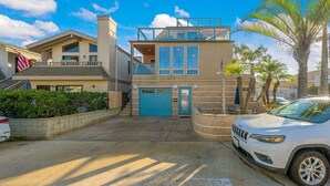 A modern two-story building with a blue garage door, a balcony, and a car parked in front. - Mission Bay Beach House/Roof-Top Deck/Parking (San Diego)
