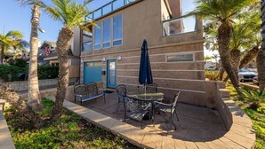 A modern building with a patio area featuring outdoor furniture and a blue umbrella. - Mission Bay Beach House/Roof-Top Deck/Parking (San Diego)
