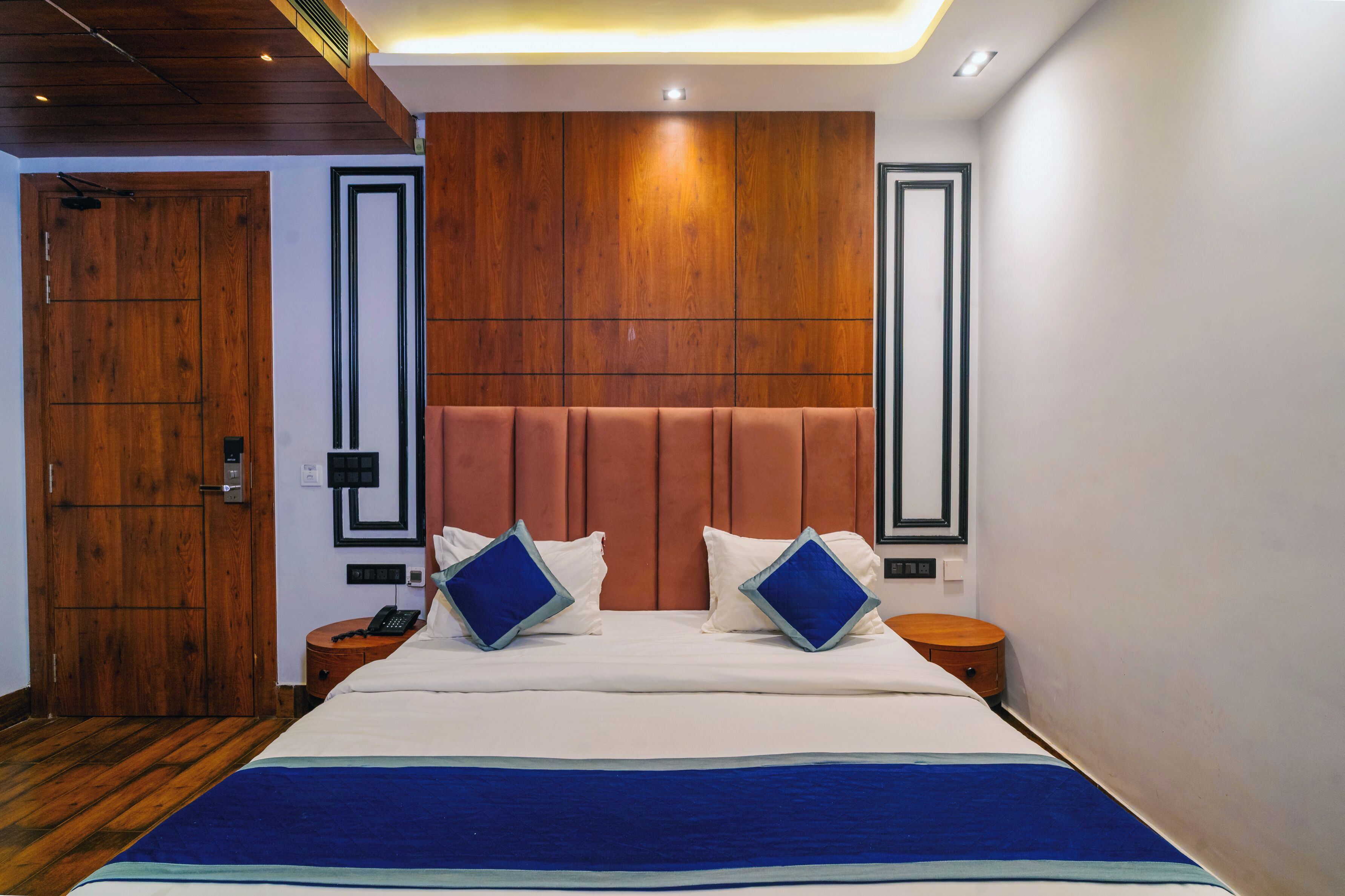 A hotel room with a wooden door, a bed with a headboard, two bedside tables, and a nightstand.