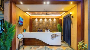 A reception desk with a clock, two receptionists, and a patterned wall behind them. - Hotel Sky Inn (Lucknow)
