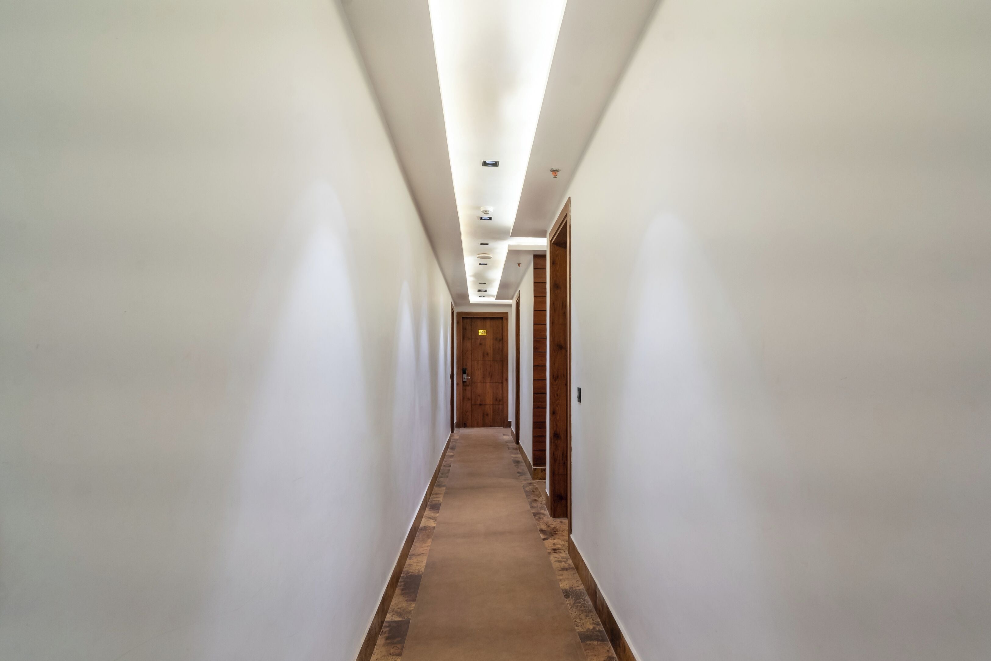 Un largo pasillo estrecho con paredes blancas y piso de madera, que conduce a una puerta al final.