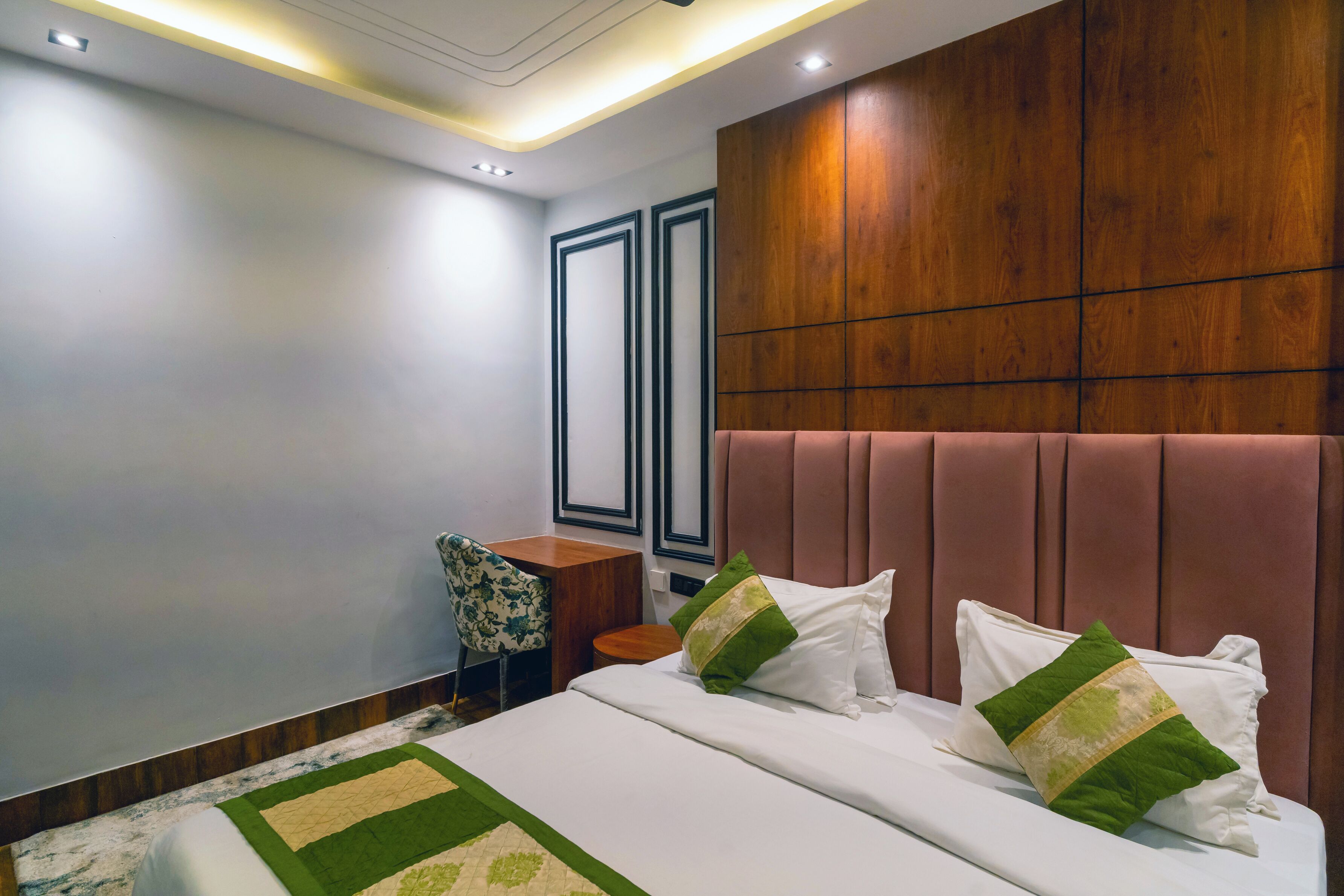 A modern hotel room with a large bed, a wooden headboard, a desk, and a chair.