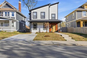 A two-story residential house with a front porch, a small tree, and a wooden fence. - Family 4BR Retreat with Games and Fun for ALL (Indianapolis)