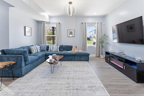A modern living room with a sectional sofa, a coffee table, a TV, and a fireplace. - Family 4BR Retreat with Games and Fun for ALL (Indianapolis)