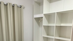 Ein Schlafzimmer mit einem Bett, weißen Vorhängen und einem weißen Kleiderschrank mit mehreren Regalen.