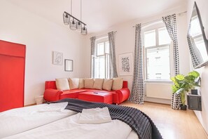 A modern bedroom with a red sofa, a large bed, and a window with polka dot curtains. - Affordable 3BR Apartment Rathausplatz (Vienna)
