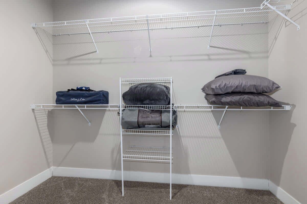 Ein begehbarer Kleiderschrank mit Metallregalen, einer Kleiderstange und einer Aufbewahrungstasche.