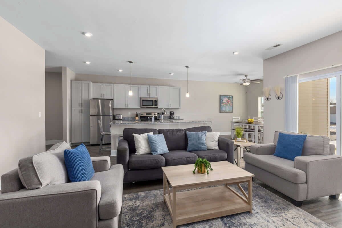 A modern living room with two grey sofas, a wooden coffee table, and a kitchen in the background.