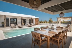 Ein moderner Poolbereich im Freien mit Holztisch und -stühlen, Liegestühlen und einer Pergola.