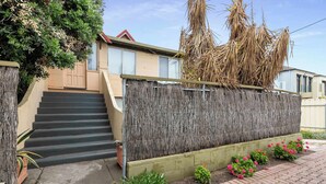 Un edificio residenziale con una scala che conduce a una porta, un muro con lamelle verticali e un giardino con fiori e piante.