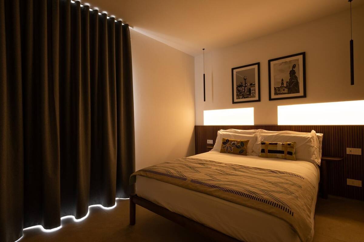 Une chambre d’hôtel avec un grand lit, des rideaux occultants, une tête de lit dotée d’un éclairage intégré et deux tableaux encadrés accrochés au mur.