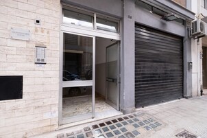 A building entrance with a closed shutter, a tiled pavement, and a sign on the wall.