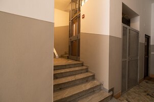 Un escalier avec une rampe en métal, un détecteur d’incendie et une porte munie d’une moustiquaire.