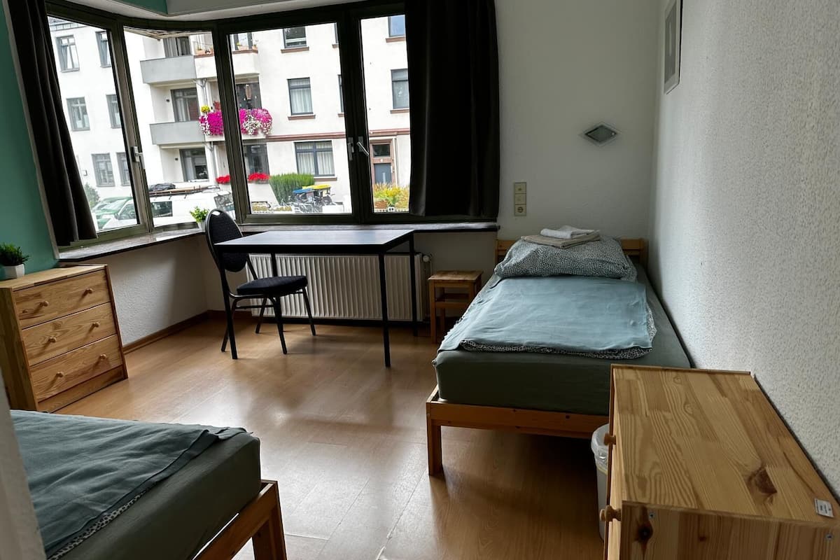Ein kleiner, kompakter Raum mit Schreibtisch, zwei Einzelbetten, einem Sessel und einer Heizung.