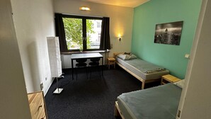 A small, compact room with a bed, a desk with a chair, and a radiator. - Hotel Grünewald chs (Hannover)