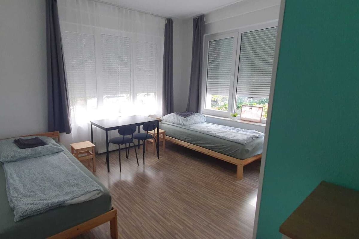 Ein kleiner, gut beleuchteter Raum mit zwei Einzelbetten, einem Schreibtisch und Stühlen.