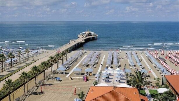 A beach with rows of umbrellas and sun loungers, a pier extending into the sea, and a clear sky. - Camaiore - Cozy Home Between Alps and Sea for Families and Groups (Camaiore)