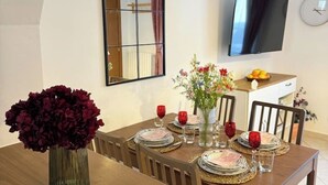 A dining area with a wooden table set for four, a vase of flowers, and a television mounted on the wall. - Camaiore - Cozy Home Between Alps and Sea for Families and Groups (Camaiore)