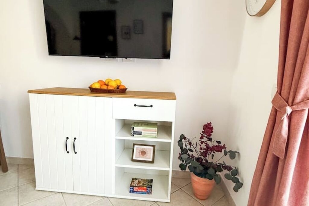 A white wardrobe with a wooden top shelf, a flat-screen TV mounted above it, and a potted plant beside the wardrobe.