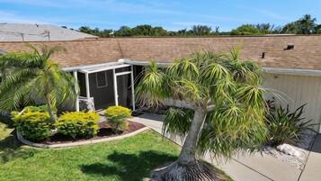 A residential backyard with a covered patio, palm trees, and a brick wall.