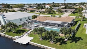 A residential property with a swimming pool, a covered patio, and a dock extending into a body of water. - Coral Sunshine - large south terrace with pool/spa (Cape Coral)