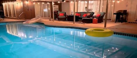An indoor swimming pool with a slide, lounge chairs, and a yellow floatation device.