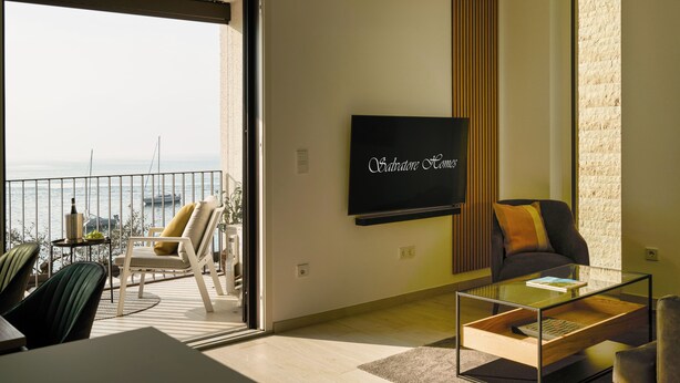 Uma sala de estar moderna com uma TV grande, uma varanda com vista para o mar e um espaço de estar acolhedor.