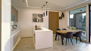 Uma cozinha moderna com uma ilha central, área de refeições com duas cadeiras e uma grande porta de vidro deslizante que dá para um espaço ao ar livre.