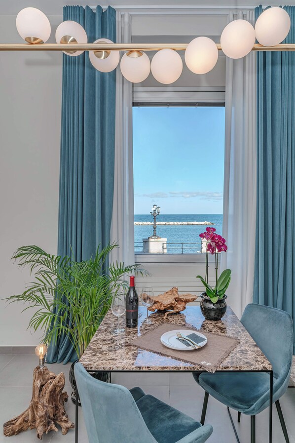 A dining area with a view of the sea, featuring a table with chairs, a bottle of wine, a plate, and a potted plant. - Alta Marea Apulia—Sea View   (Bari)