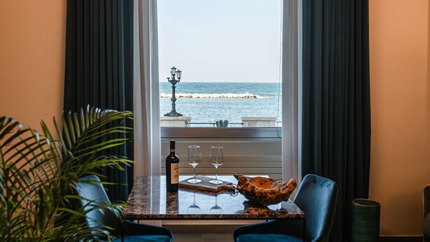 A dining area with a view of the sea, featuring a table with chairs, a bottle of wine, and a glass. - Alta Marea Apulia sea view (Bari)