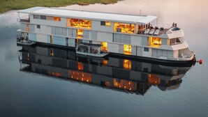 A large, multi-level houseboat with a flat roof, multiple decks, and a covered front deck. - Zambezi Queen by Mantis  (Kasika)
