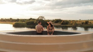 A couple sitting on a circular outdoor platform with a view of a body of water and surrounding vegetation. - Zambezi Queen by Mantis  (Kasika)