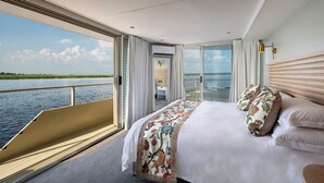A modern hotel room with a large bed, a view of the water, and a balcony. - Zambezi Queen by Mantis  (Kasika)