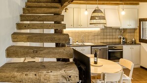 Un escalier en bois mène à une cuisine dotée de meubles blancs, d’une table à manger et de luminaires suspendus.
