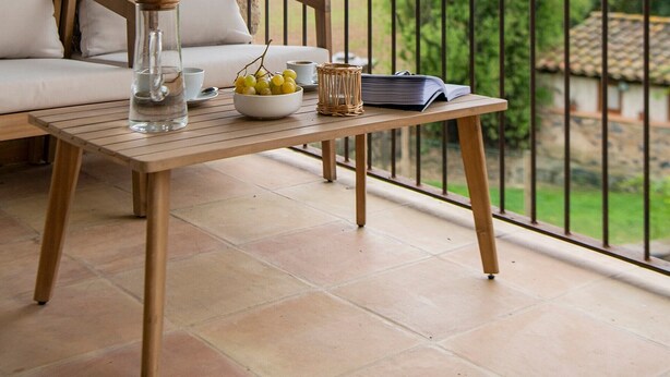Un balcon avec une table en bois, un panier en osier et un saladier rempli de fruits.