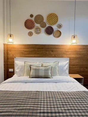 A neatly made bed with a plaid bedspread, a wooden headboard, and a wall decorated with various textured wall art pieces. - Ease at Sathorn and Co-working Space (Bangkok)