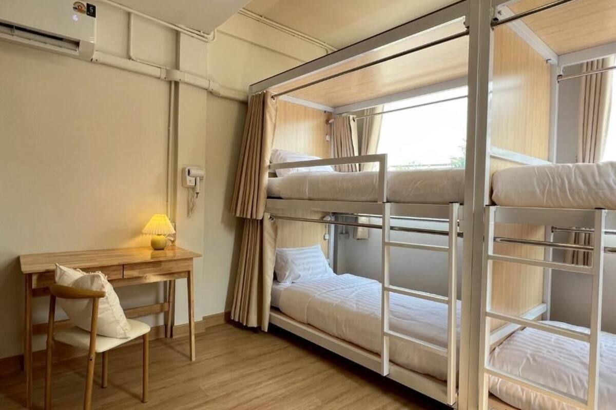 Dormitorio con literas, un escritorio, una silla, una lámpara y un equipo de aire acondicionado.