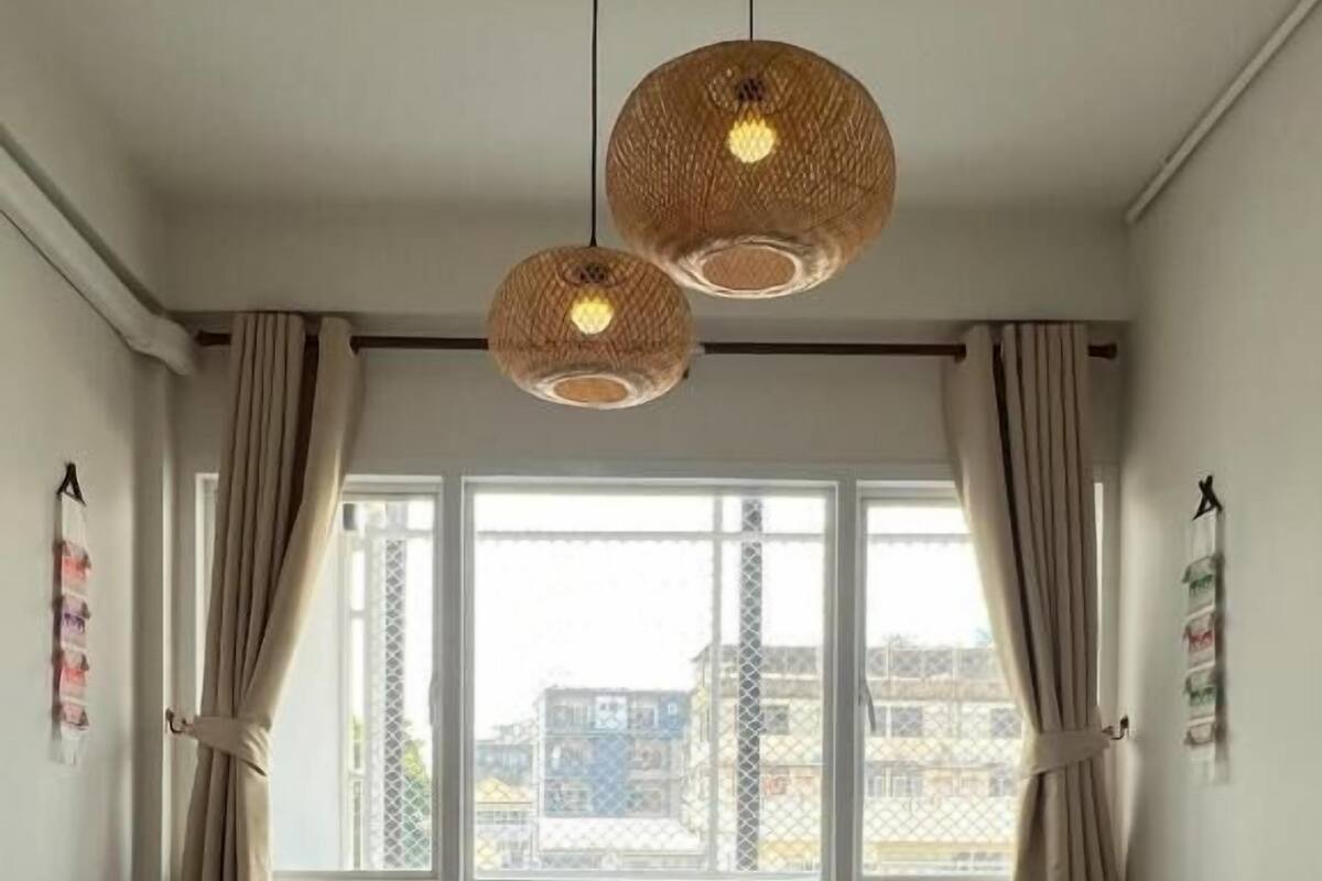 Un dormitorio con una cama grande, dos lámparas colgantes, una ventana con cortinas y vistas a edificios.