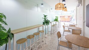 Un intérieur moderne avec un long comptoir, des tabourets de bar, des tables rondes, des chaises en osier et des lampes en osier suspendues.