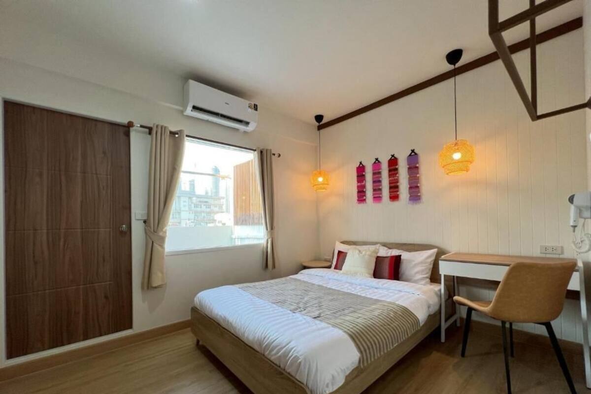 Un dormitorio con cama, escritorio y silla. Hay una ventana con cortinas, un equipo de aire acondicionado y luces empotradas.