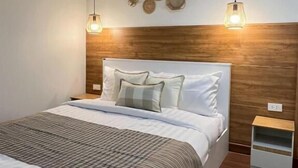 Une chambre à coucher bien aménagée, avec une tête de lit en bois, un lit recouvert de draps blancs, deux lampes suspendues et un mur décoré de paniers tressés.