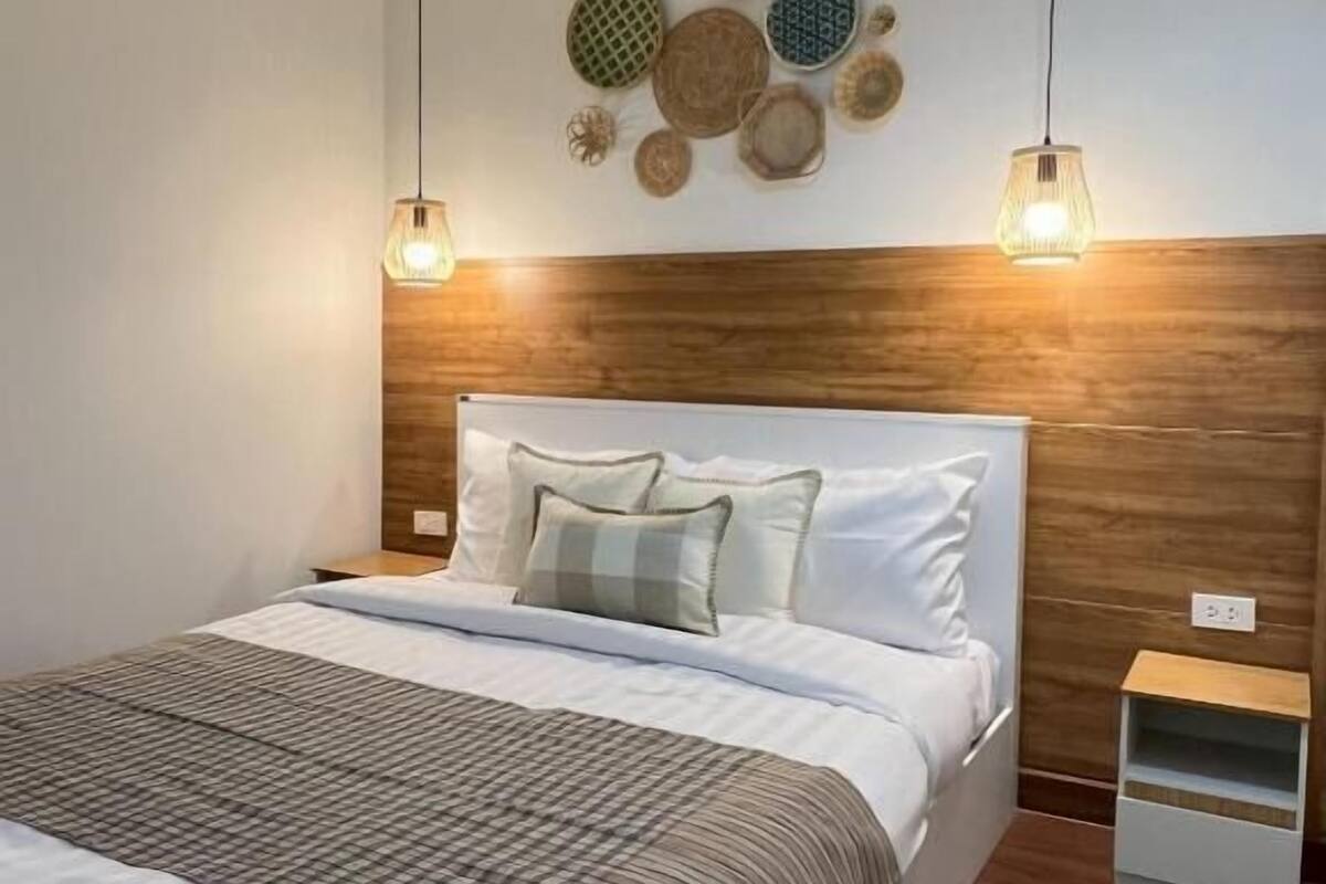 Un dormitorio ordenado con cabecera de madera, cama con ropa blanca, dos lámparas colgantes y una pared decorada con cestas tejidas.